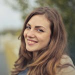 A young woman smiling warmly with a blurred outdoor background in Budapest.