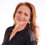 Portrait of a smiling senior woman with long hair and earrings in a black outfit.